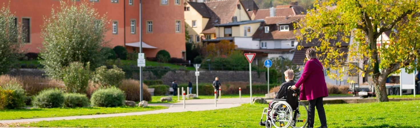 Eine Frau schiebt einen älteren Mann im Rollstuhl.